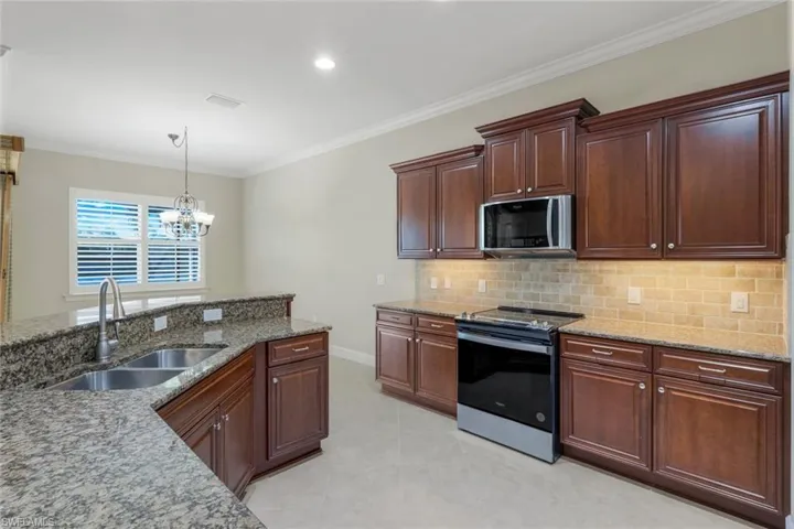 Kitchen featuring a notable chandelier, sink, ornamental molding, and stainless steel appliances