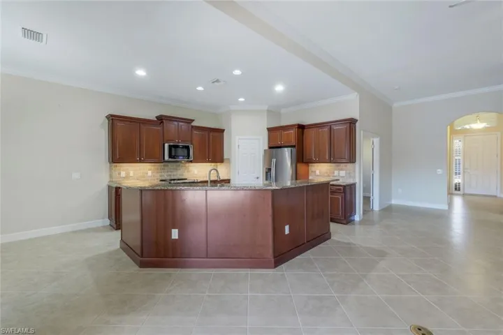 Kitchen with light tile patterned flooring, ornamental molding, stainless steel appliances, and an island with sink