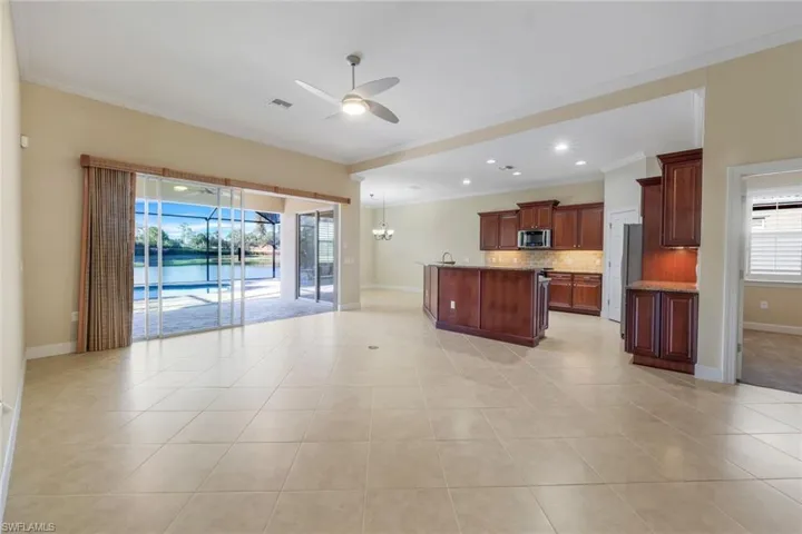 Kitchen with a kitchen island with sink, ceiling fan with notable chandelier, ornamental molding, tasteful backsplash, and stainless steel appliances