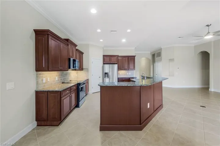 Kitchen featuring range with electric cooktop, ceiling fan, a kitchen island with sink, stainless steel refrigerator with ice dispenser, and decorative backsplash