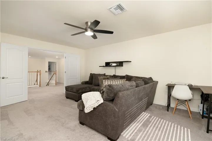 Spacious carpeted room featuring a ceiling fan with integrated lighting, a built-in wall shelf, and double doors opening to a staircase