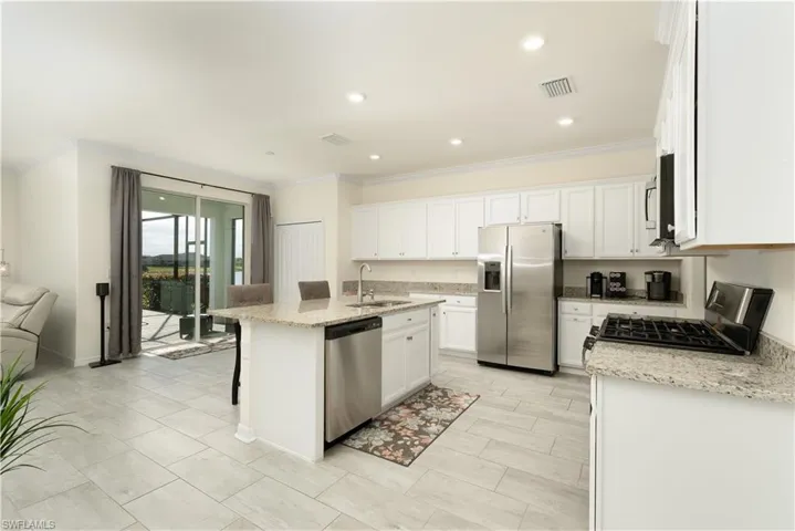 Open-concept kitchen featuring white cabinetry, granite countertops, stainless steel appliances, a center island with seating, and light-toned tile flooring