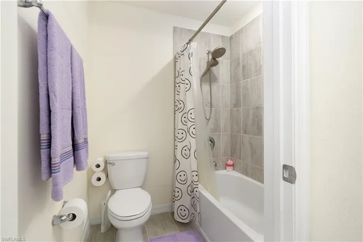 Bathroom featuring a full tub/shower combination with light gray tile surround, a white toilet, and light-toned flooring