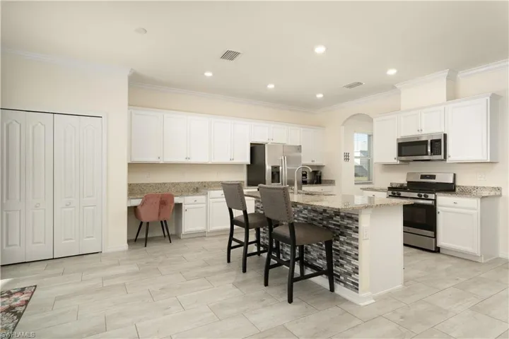 Open-concept kitchen featuring extensive white cabinetry, stainless steel appliances, a central island with a multi-tone tile facade, and wood-finish flooring