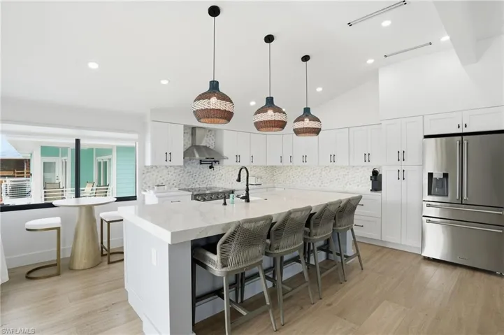 Kitchen featuring high end refrigerator, a breakfast bar area, pendant lighting, light wood-style flooring, and decorative backsplash Virtually Edited