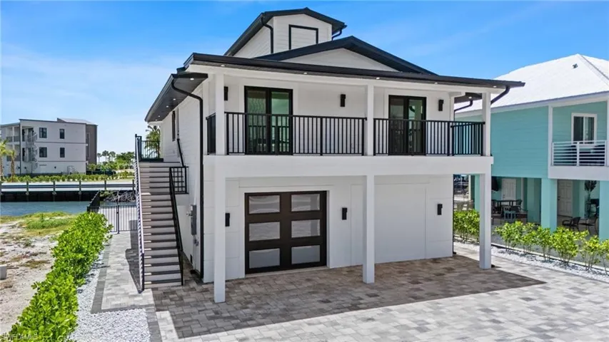 Coastal home with stairs, an attached garage, a water view, and a balcony- Virtually Edited