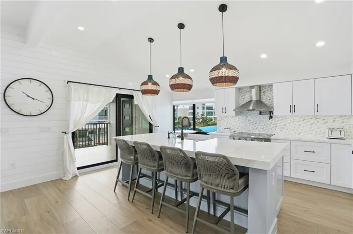Kitchen featuring white cabinetry, a breakfast bar area, decorative light fixtures, light wood-style floors, and lofted ceiling Virtually Edited