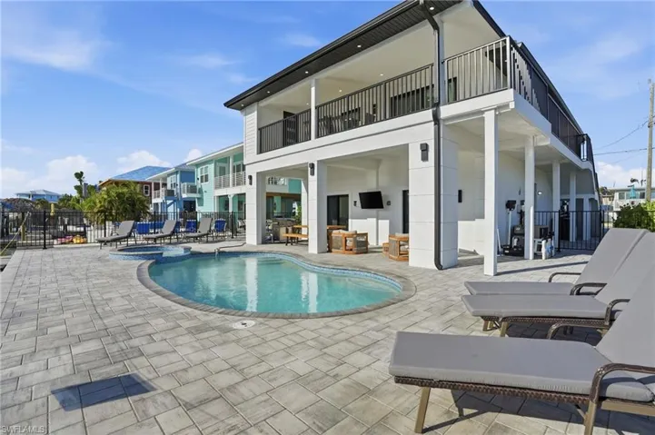 Back of property featuring a patio area, a pool with connected hot tub, a balcony, and an outdoor hangout area Virtually Edited