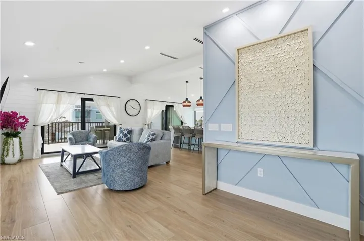 Living area featuring lofted ceiling, light wood-style flooring, recessed lighting, and wooden walls Virtually Edited