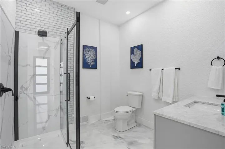 Bathroom featuring a marble finish shower, vanity, light marble finish flooring, and recessed lighting virtually edited