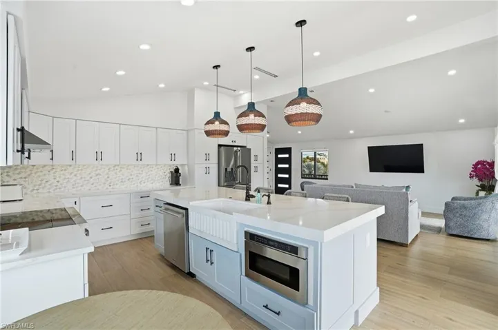 Kitchen with backsplash, pendant lighting, white cabinets, light wood-style floors, and high vaulted ceiling Virtually Edited