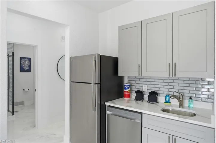 Kitchen featuring stainless steel dishwasher, light stone counters, backsplash, and light epoxy flooring Virtually edited