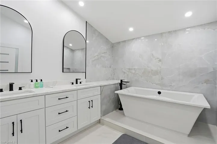 Full bathroom featuring tile walls, double vanity, a freestanding tub, and recessed lighting virtually edited