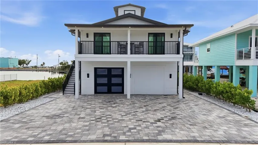 Raised beach house with decorative driveway, an attached garage, and stairway Virtually Edited