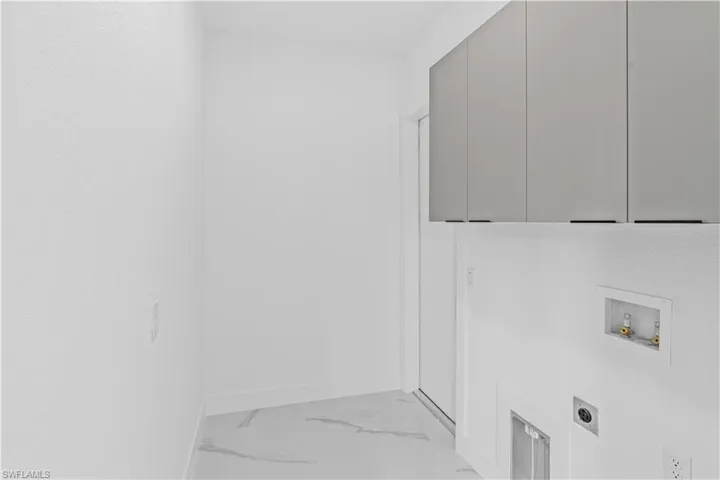 Clothes washing area featuring hookup for an electric dryer, baseboards, washer hookup, cabinet space, and light marble finish flooring