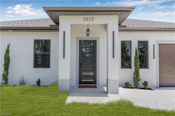 Entrance to property with roof with shingles, stucco siding, and a yard