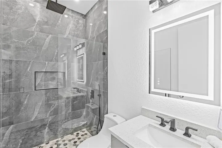 Full bath featuring a textured wall, toilet, tiled shower, and vanity