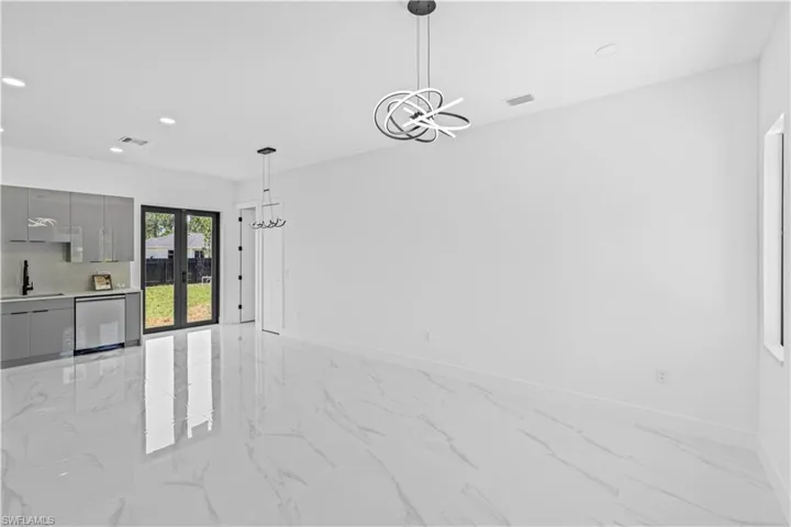 Unfurnished dining area featuring recessed lighting, light marble finish floors, a chandelier, a sink, and baseboards