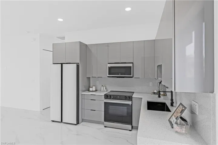 Kitchen with gray cabinets, stainless steel appliances, a sink, light marble finish flooring, and modern cabinets