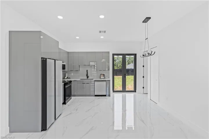 Kitchen with gray cabinetry, modern cabinets, a sink, appliances with stainless steel finishes, and light marble finish flooring