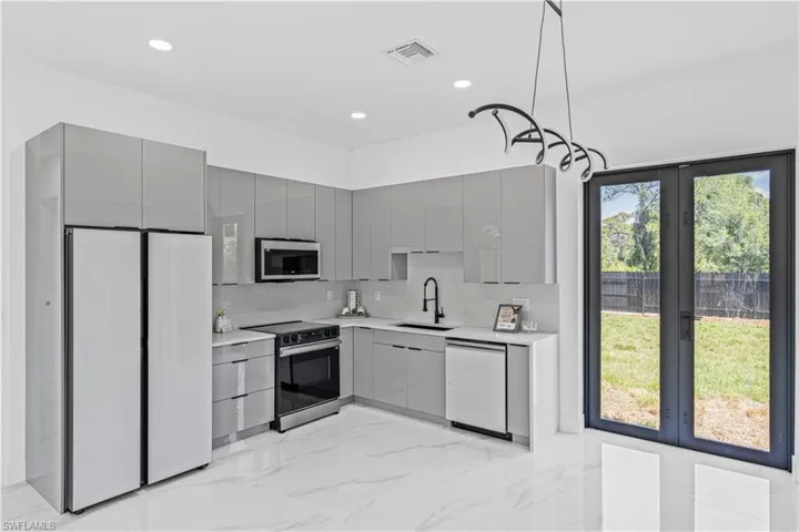 Kitchen featuring stainless steel appliances, gray cabinetry, a sink, light marble finish flooring, and light countertops