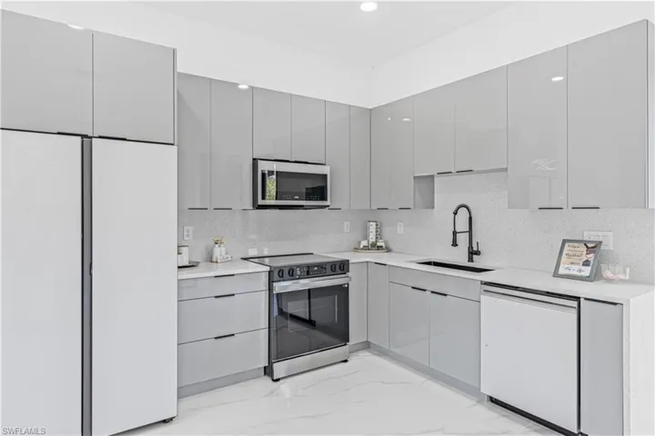 Kitchen featuring appliances with stainless steel finishes, a sink, gray cabinetry, light marble finish flooring, and recessed lighting