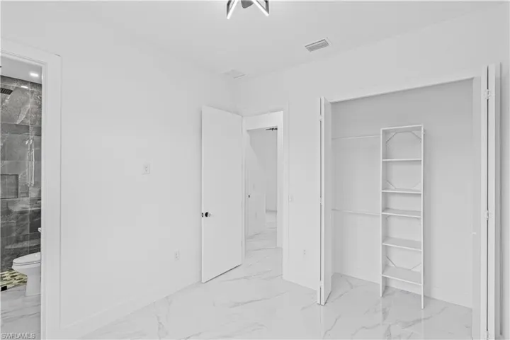 Unfurnished bedroom with marble finish floors, baseboards, a closet, and ensuite bathroom
