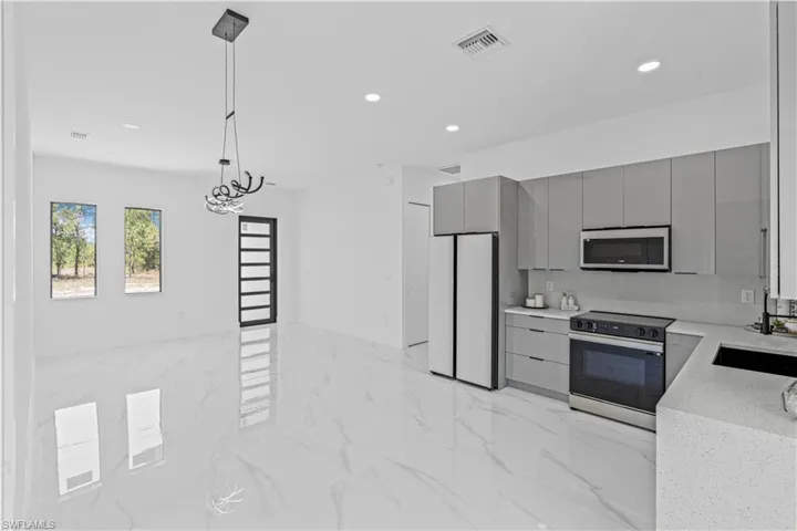 Kitchen with gray cabinets, appliances with stainless steel finishes, a sink, modern cabinets, and light marble finish flooring