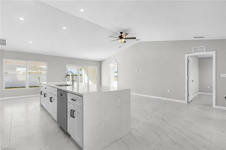 Kitchen featuring white cabinetry, light stone counters, light marble finish floors, open floor plan, and vaulted ceiling