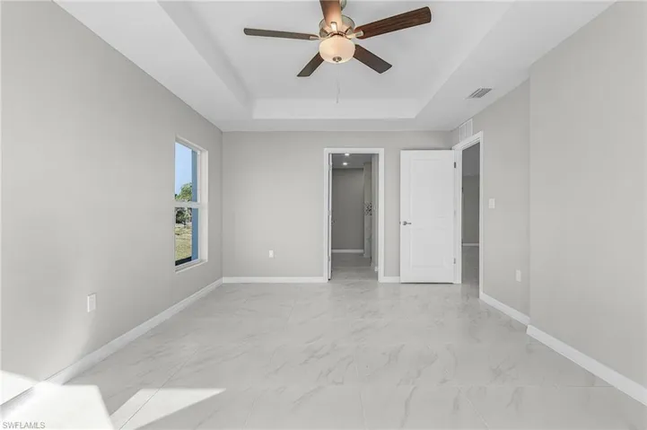 Unfurnished bedroom with light marble finish flooring, ceiling fan, and a raised ceiling