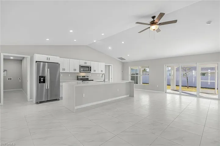 Kitchen featuring appliances with stainless steel finishes, a kitchen island with sink, open floor plan, lofted ceiling, and white cabinetry
