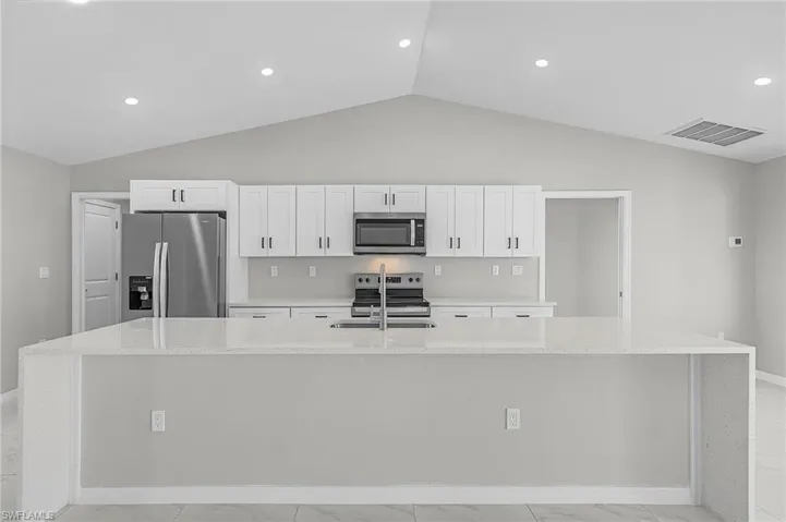 Kitchen with light stone countertops, stainless steel appliances, a large island with sink, white cabinetry, and light marble finish flooring