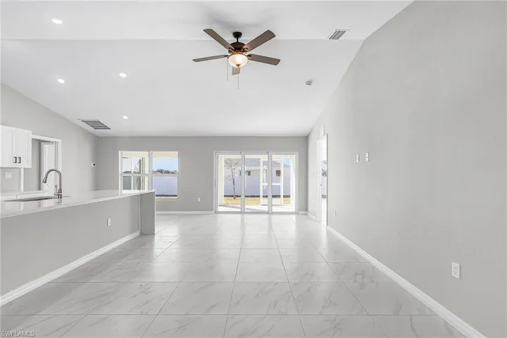 Unfurnished living room featuring light marble finish floors, ceiling fan, lofted ceiling, and recessed lighting