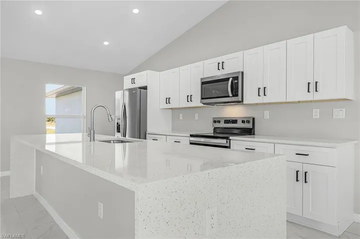 Kitchen featuring light stone countertops, stainless steel appliances, lofted ceiling, white cabinets, and recessed lighting