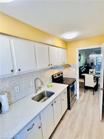 Kitchen with electric range, white cabinets, light wood-style flooring, decorative backsplash, and a chandelier