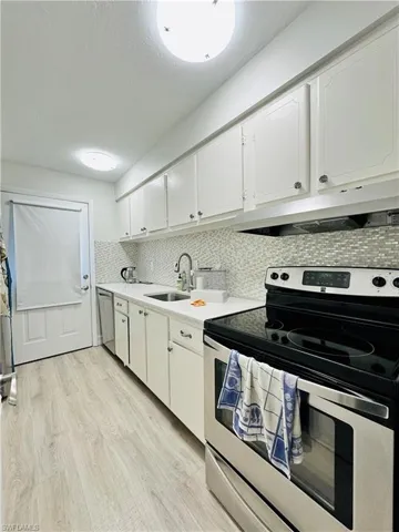 Kitchen with stainless steel appliances, white cabinets, light wood-style flooring, under cabinet range hood, and a textured ceiling