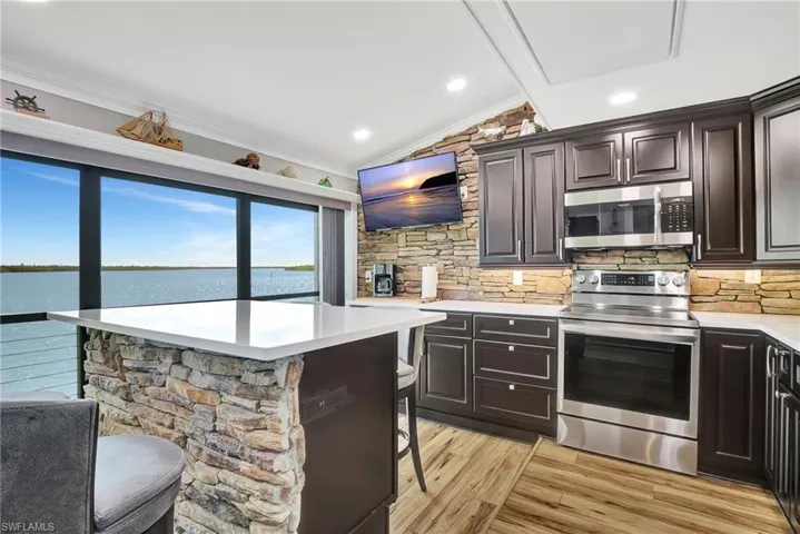 Kitchen with a kitchen breakfast bar, crown molding, decorative backsplash, light hardwood / wood-style floors, and stainless steel appliances