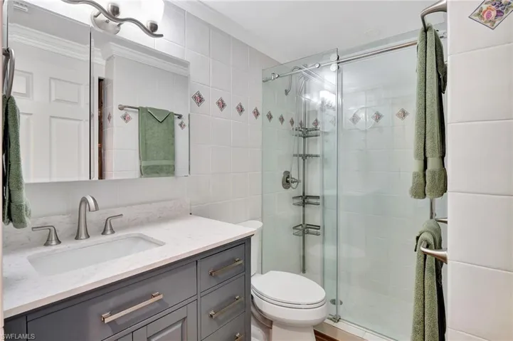 Bathroom with walk in shower, vanity, toilet, and tile walls
