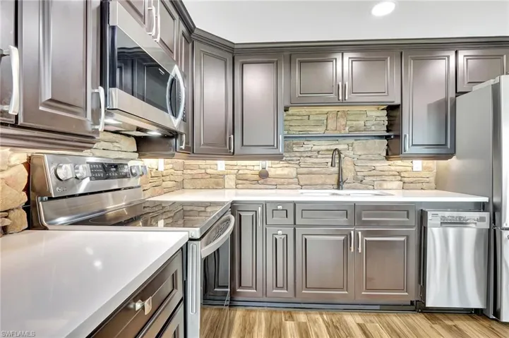 Kitchen featuring stone backsplash, sink, luxury vinyl floors, and appliances with stainless steel finishes