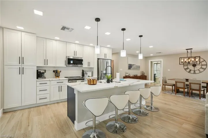 Kitchen featuring light wood-type flooring, appliances with stainless steel finishes, white cabinetry, an island with sink, and pendant lighting