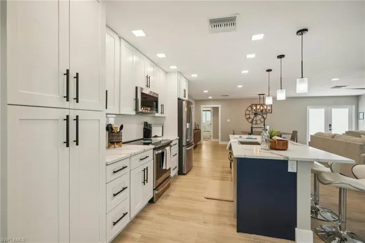 Kitchen with white cabinets, light hardwood / wood-style flooring, appliances with stainless steel finishes, light stone counters, and an island with sink