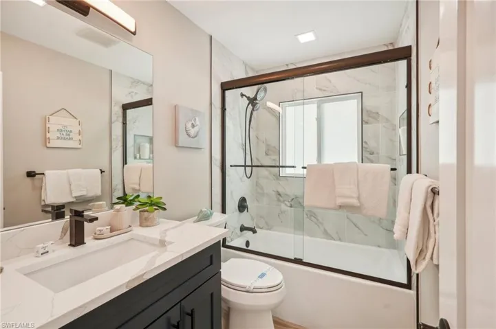 Full bathroom with enclosed tub / shower combo, toilet, and vanity