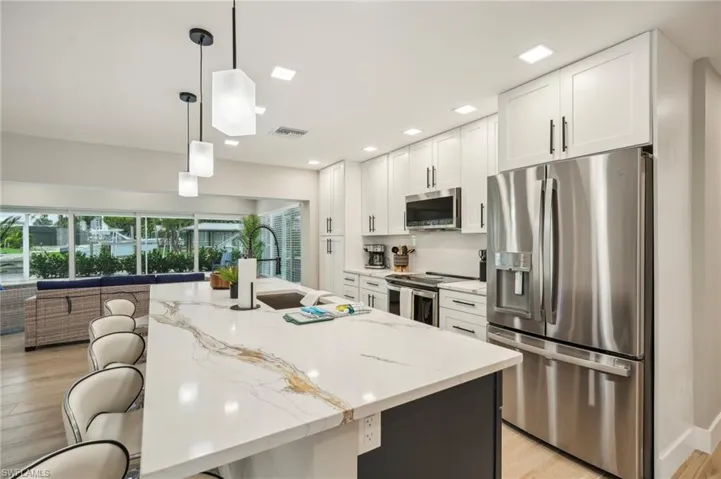 Kitchen with hanging light fixtures, light stone countertops, appliances with stainless steel finishes, and a kitchen island with sink