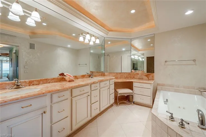 Bathroom featuring double vanity, a jetted tub, a raised ceiling, ornamental molding, and light tile patterned flooring