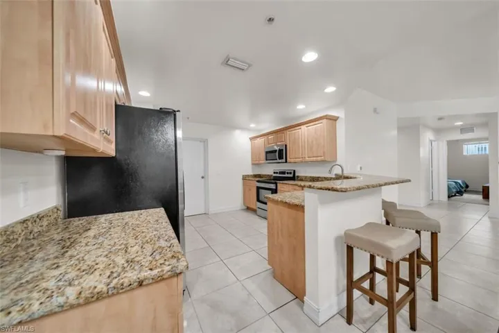Kitchen with light brown cabinetry, light tile patterned floors, light stone countertops, stainless steel appliances, and recessed lighting