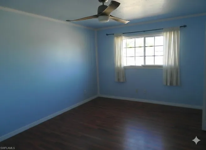 Empty room featuring dark wood-style floors, a ceiling fan, and crown molding