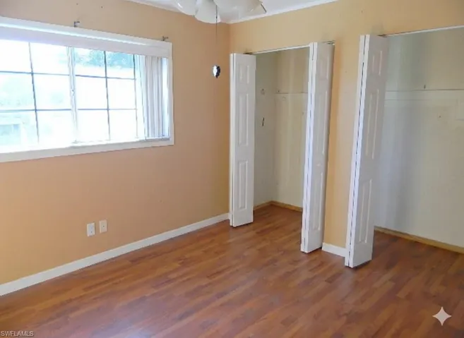 Unfurnished bedroom with multiple closets, wood finished floors, and ceiling fan