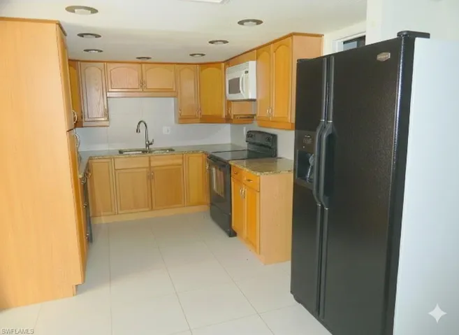 Kitchen featuring black appliances, light tile patterned floors, light wood finish cabinets, and light stone counters