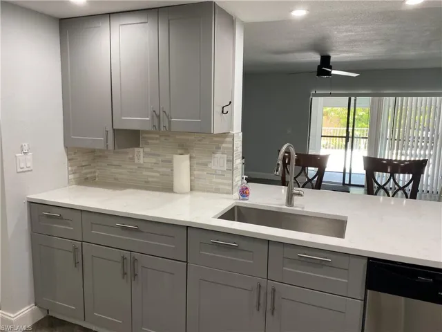 Kitchen featuring gray cabinets, light stone counters, backsplash, recessed lighting, and a textured ceiling