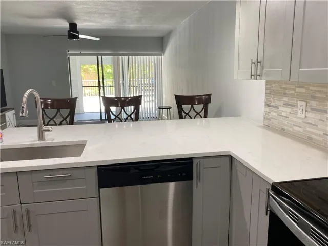 Kitchen featuring gray cabinetry, dishwasher, decorative backsplash, and light stone counters